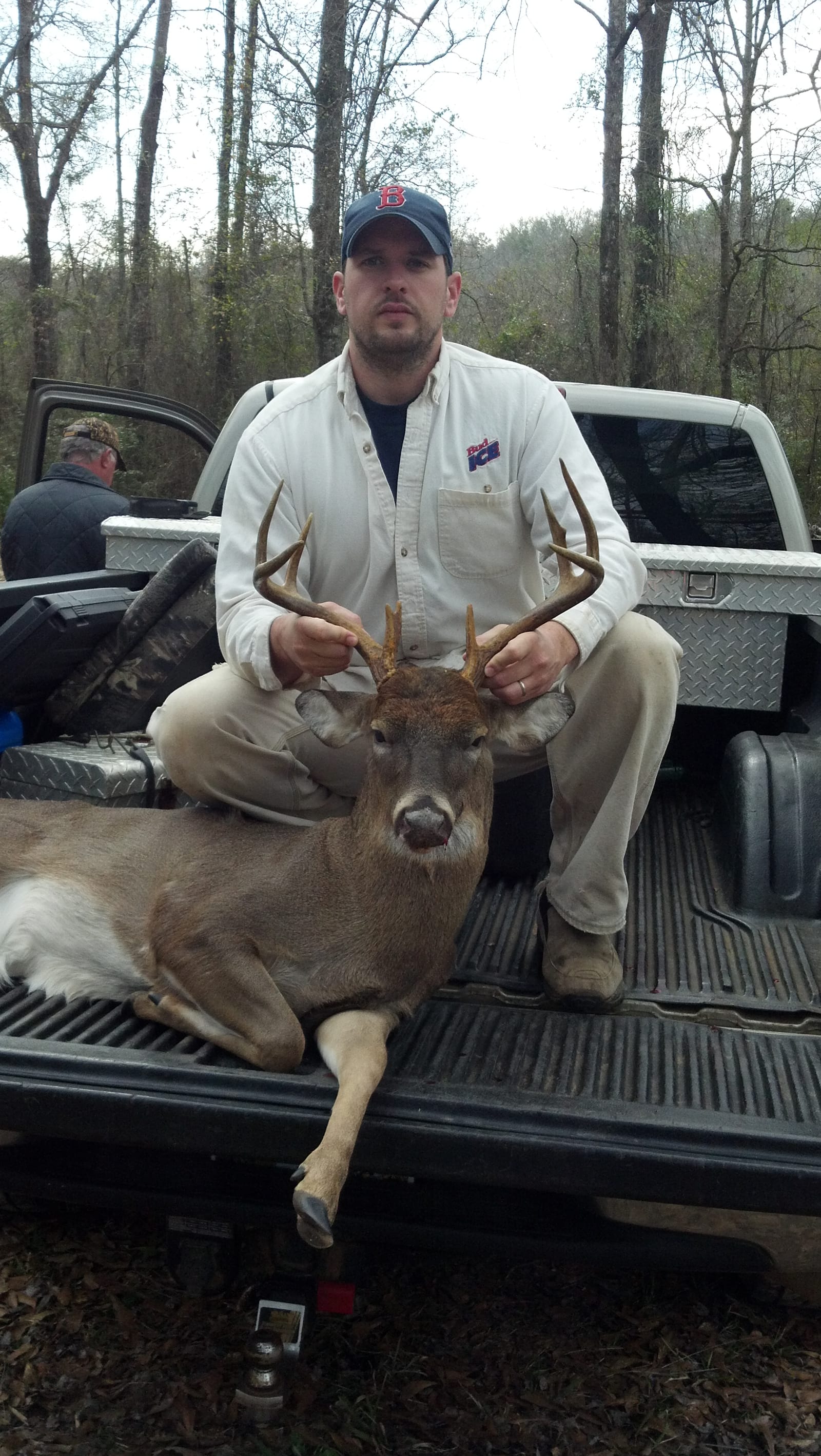 A man poses with a harvested whitetail deer in the back of a pickup truck.