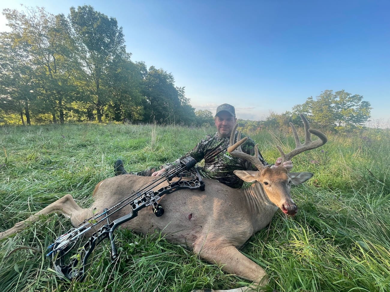 A hunter poses with a harvested whitetail deer in a grassy field.
