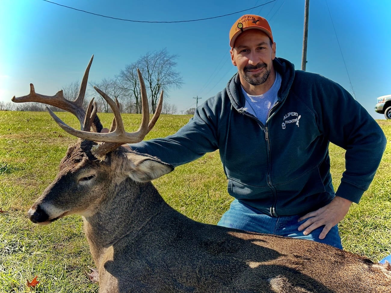 A hunter kneels next to a harvested whitetail deer in a grassy field.