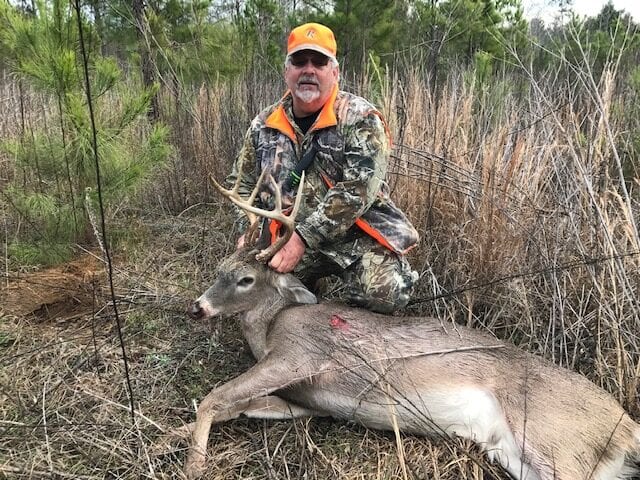 Hunter kneeling behind whitetail buck in camo