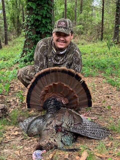 Camouflaged hunter kneeling beside harvested turkey