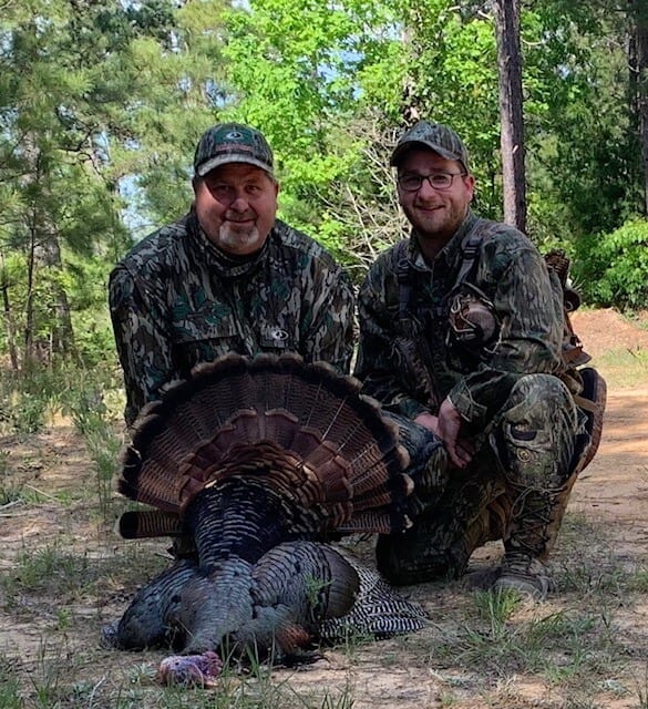 Two camouflaged hunters posing with turkey