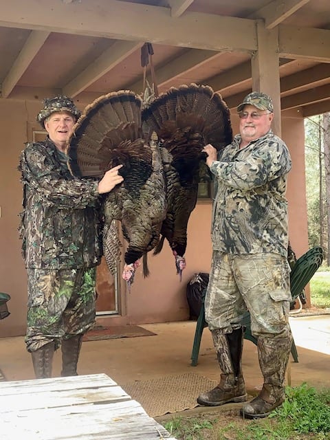 Two men holding a turkey in camouflage clothes.