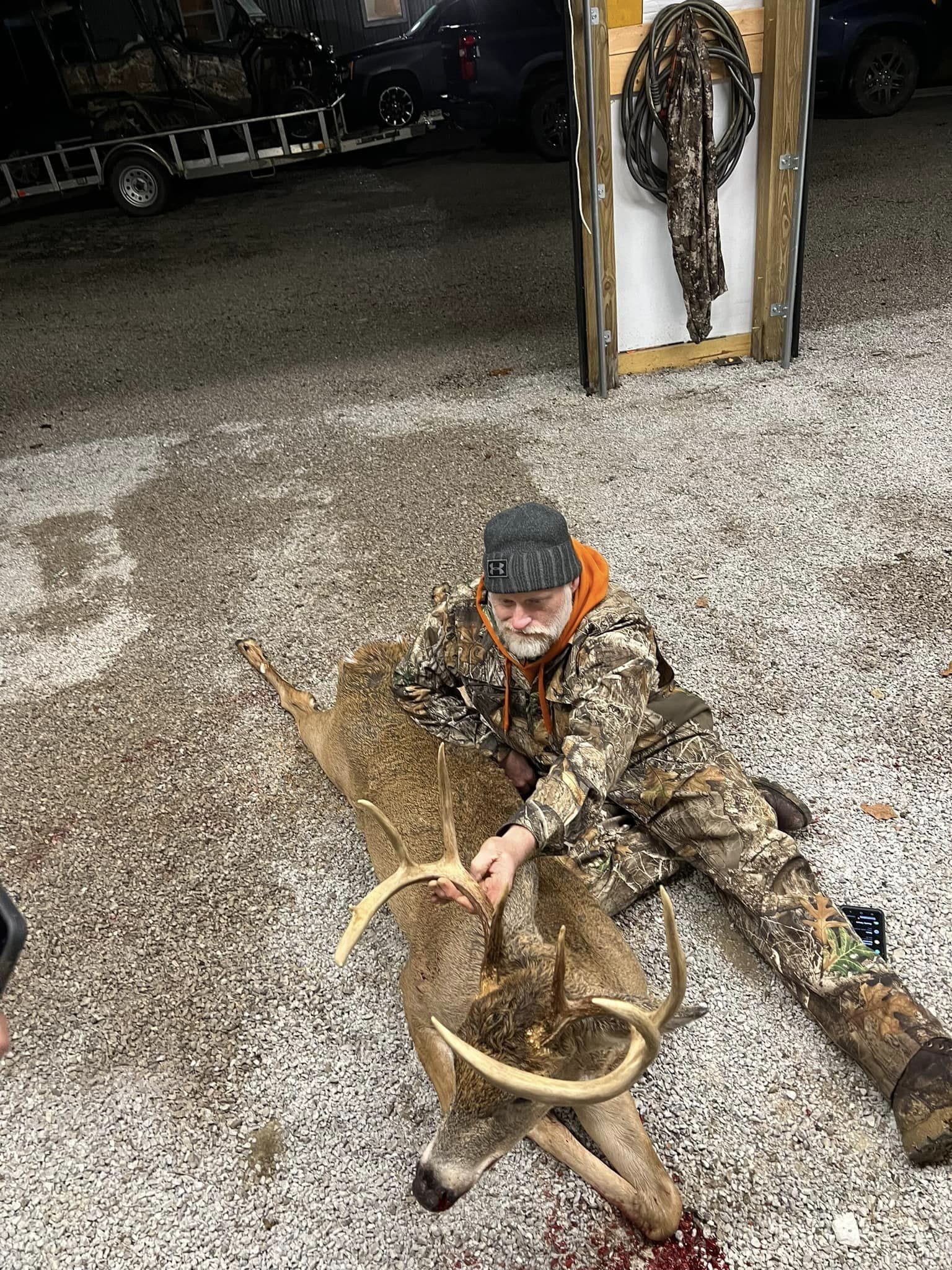 Hunter admiring a freshly harvested buck with wide antlers on a gravel lot.