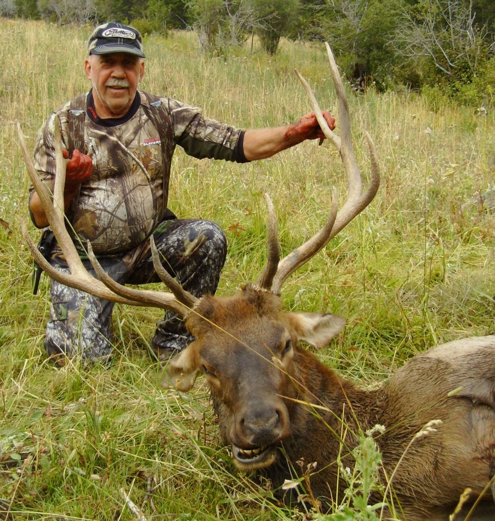 A hunter kneels next to a harvested elk in a grassy field.