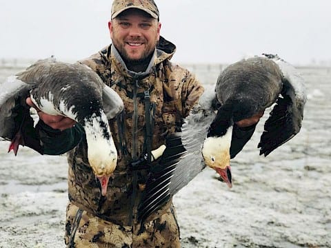 A hunter smiles while holding two harvested blue geese.