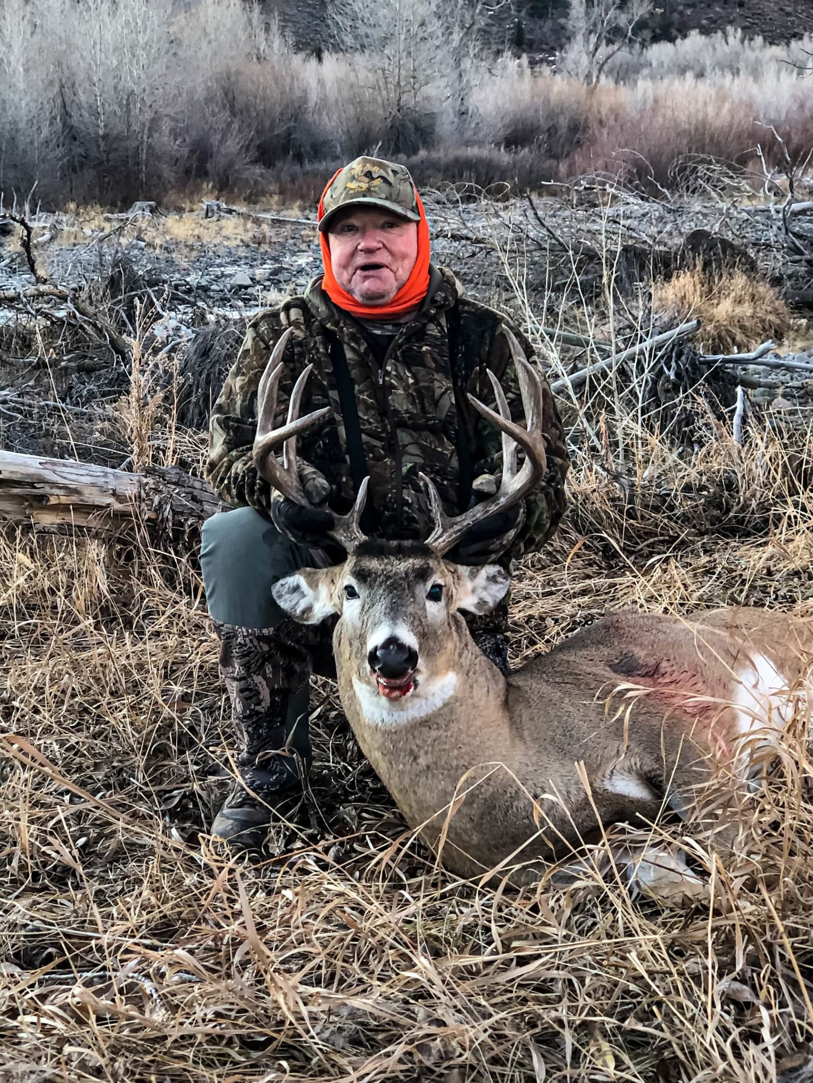 A hunter kneels next to a harvested whitetail deer in a field.