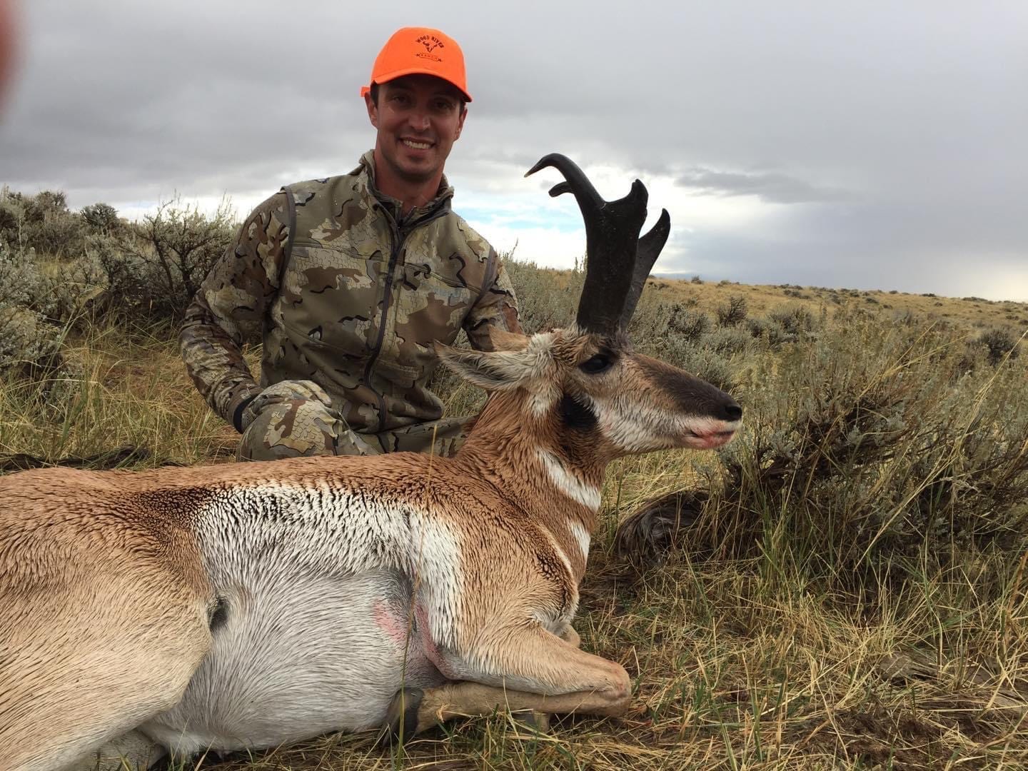 A hunter poses with a harvested pronghorn in a field.