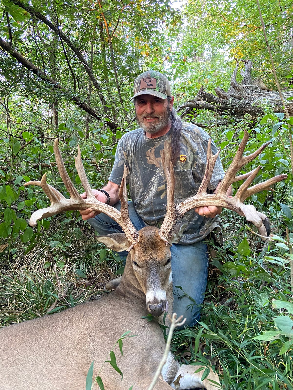 A hunter kneels next to a harvested whitetail deer in a wooded area.