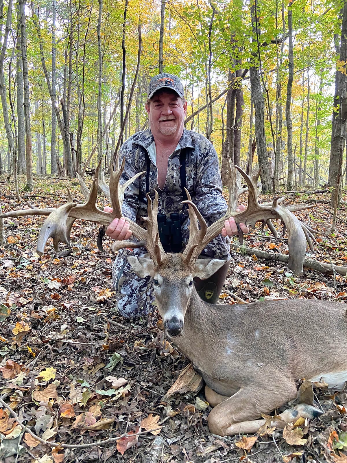 A hunter kneels behind a harvested whitetail deer in a forest.