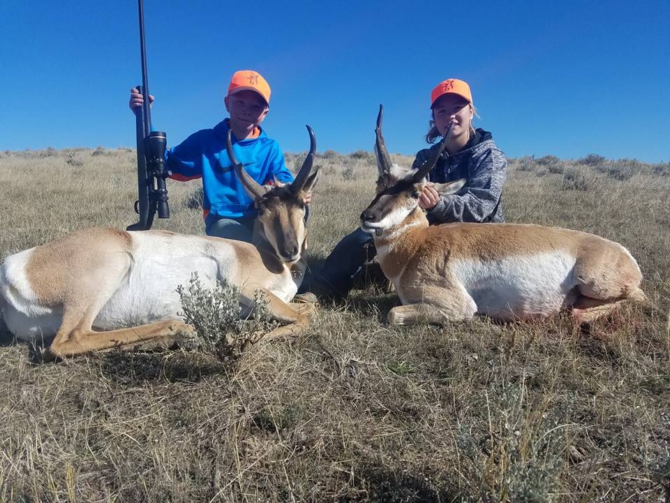 Two hunters pose with two harvested pronghorn in a field.