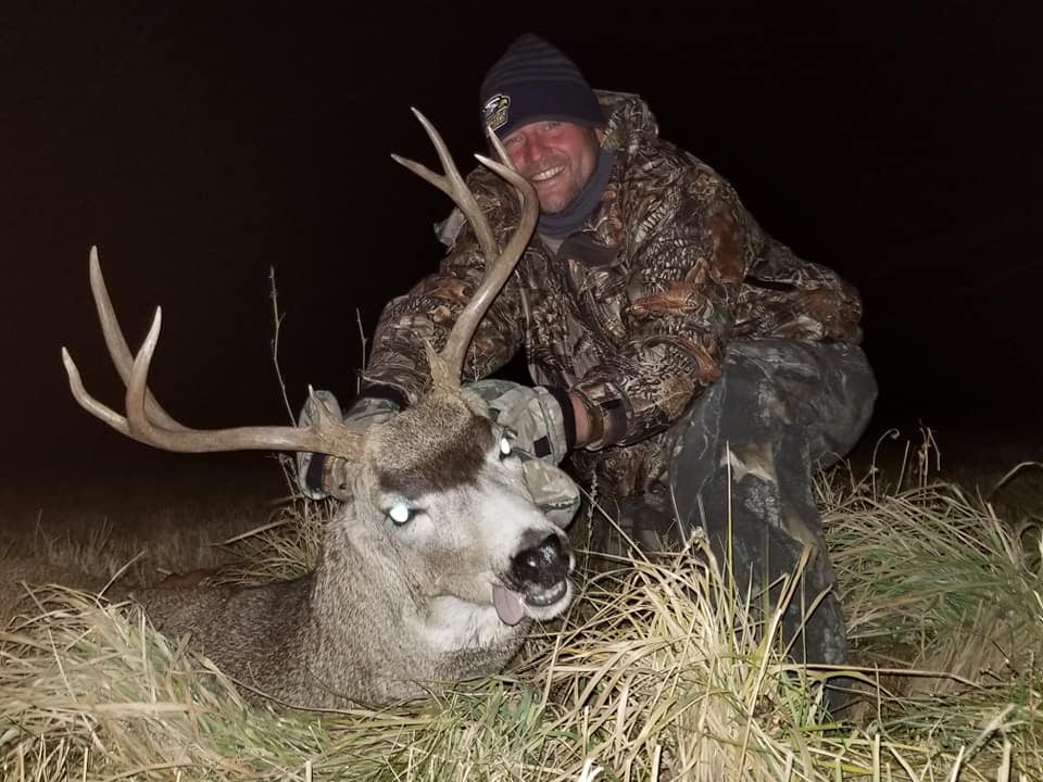 A hunter poses at night with a harvested mule deer.