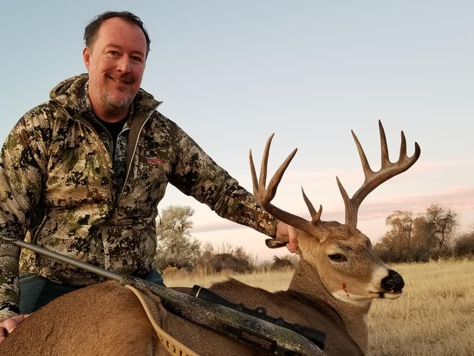 A hunter poses with a harvested whitetail deer in a field.