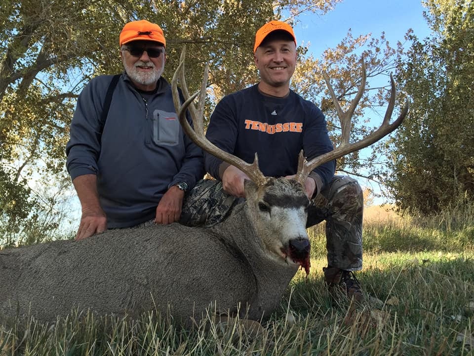 Two hunters pose with a harvested mule deer.