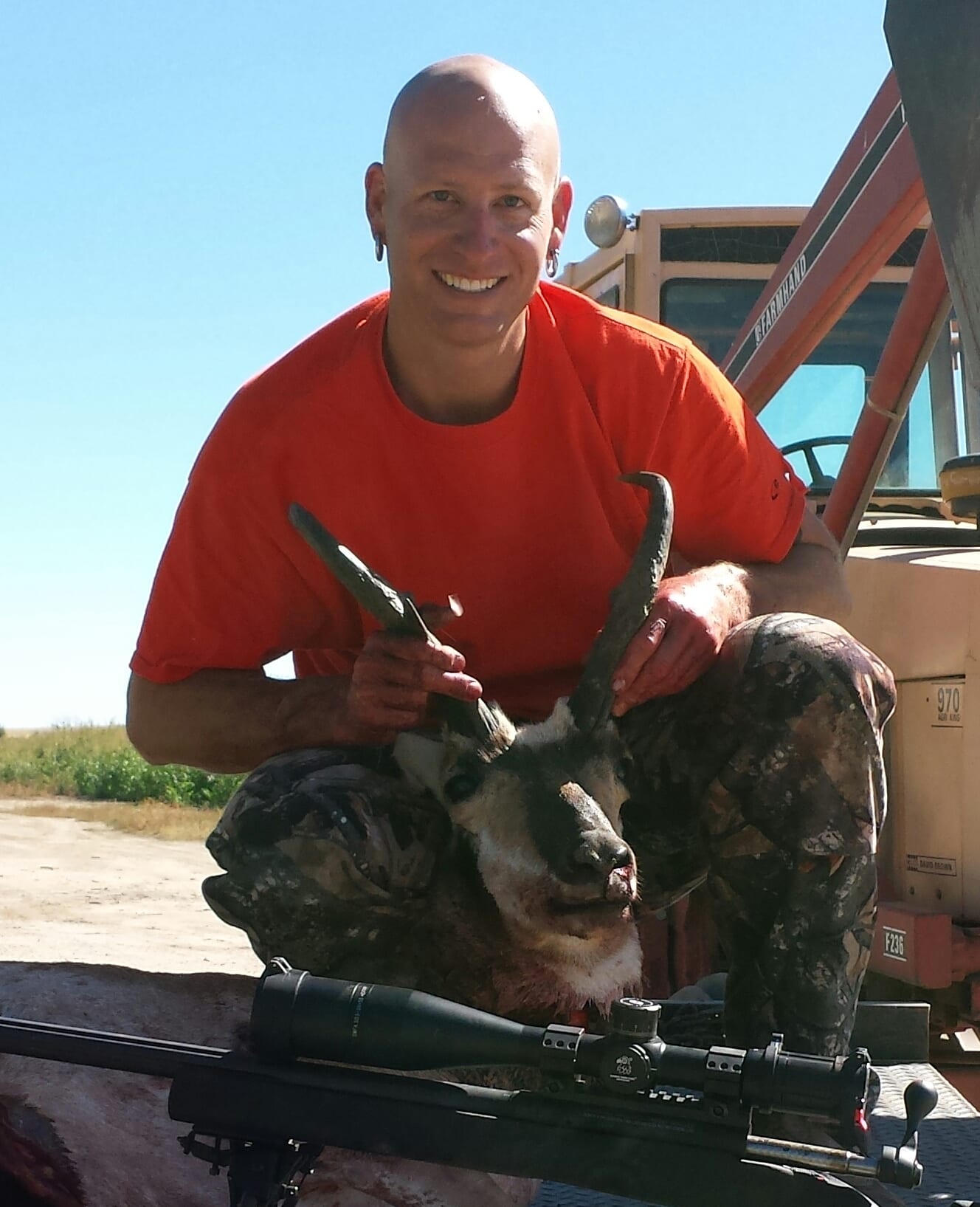 A hunter poses with a harvested pronghorn and a rifle.