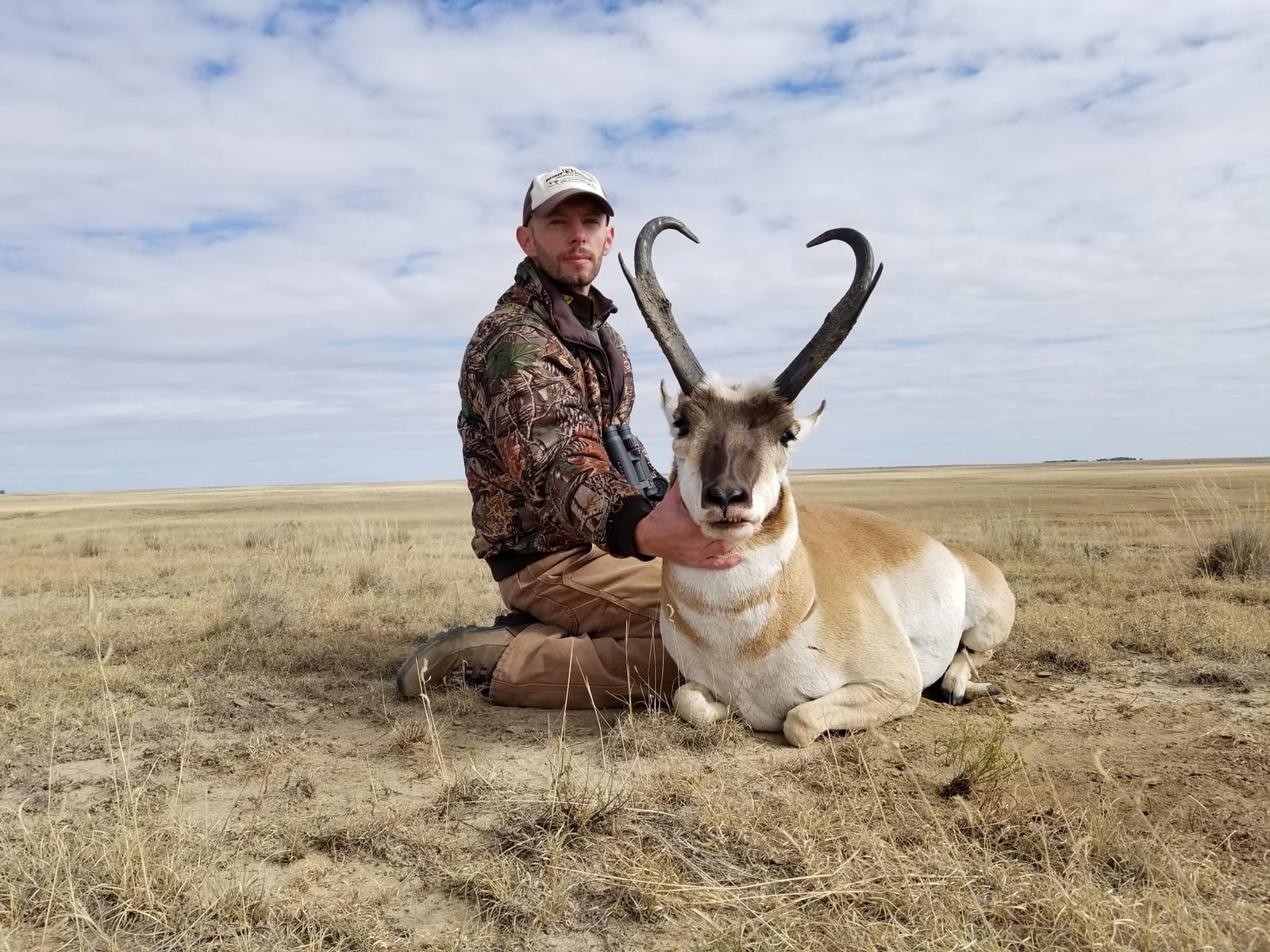 A hunter kneels in a field next to a harvested pronghorn.