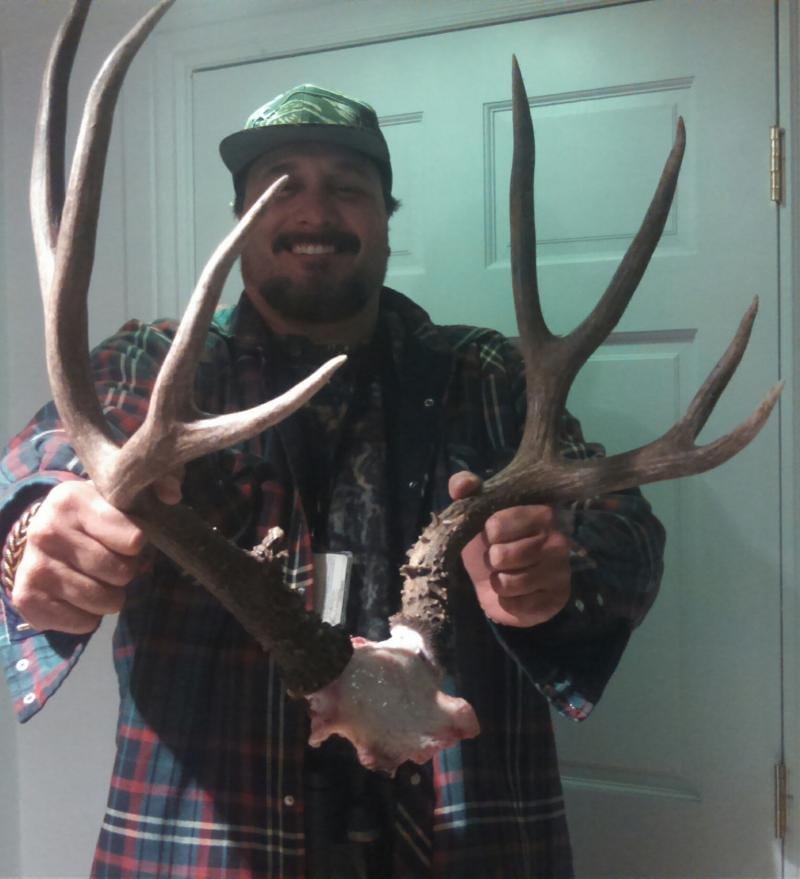 A man smiles while holding a pair of mule deer antlers with part of the skull attached.
