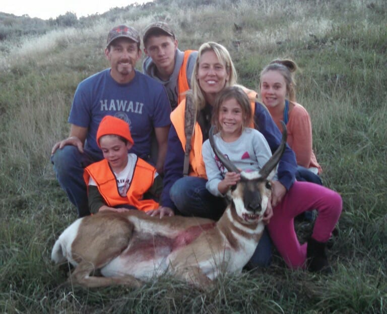 A family poses with a harvested pronghorn in a grassy field.