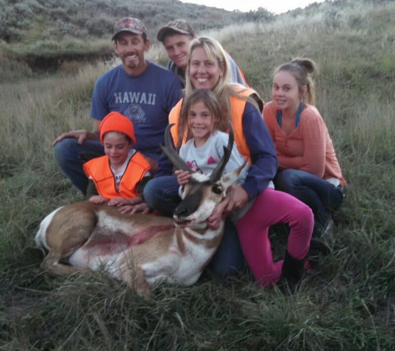 A family poses with a harvested pronghorn in a grassy field.